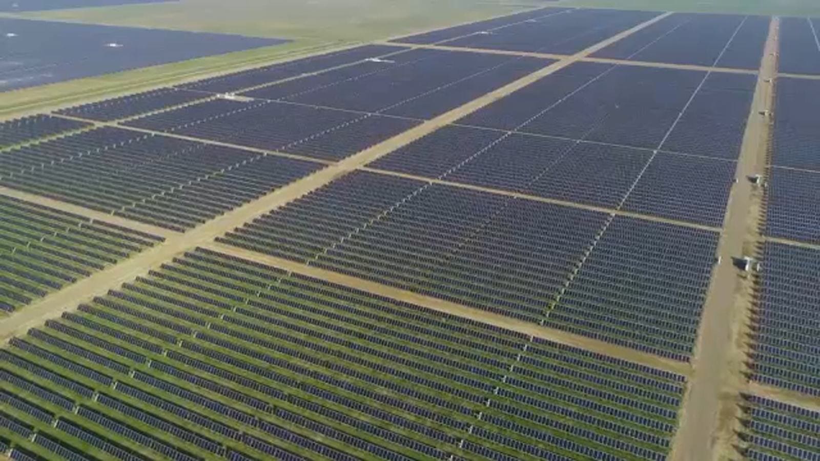 A large field of solar panels with dirt ground.